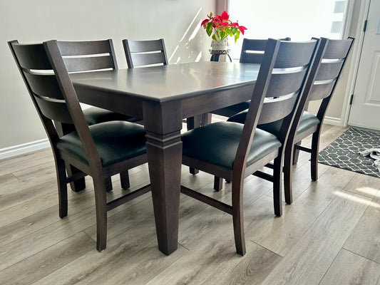 Handcrafted solid wood dining table with six dark-stained chairs and black leather seats in a modern Edmonton home
