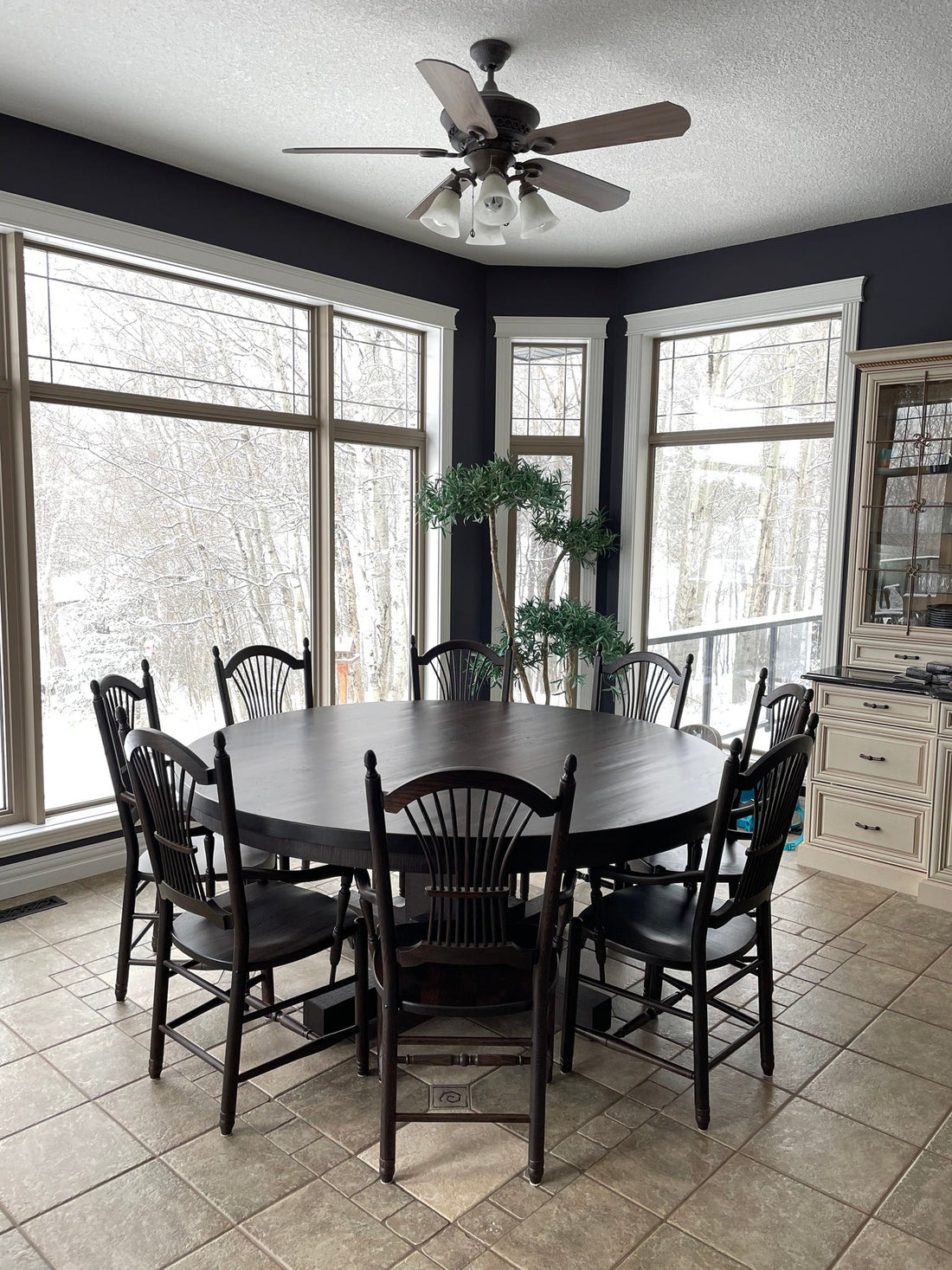 Solid wood round dining table with eight chairs in a bright Edmonton dining room overlooking a snowy landscape