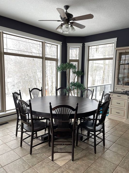 Solid wood round dining table with eight chairs in a bright Edmonton dining room overlooking a snowy landscape